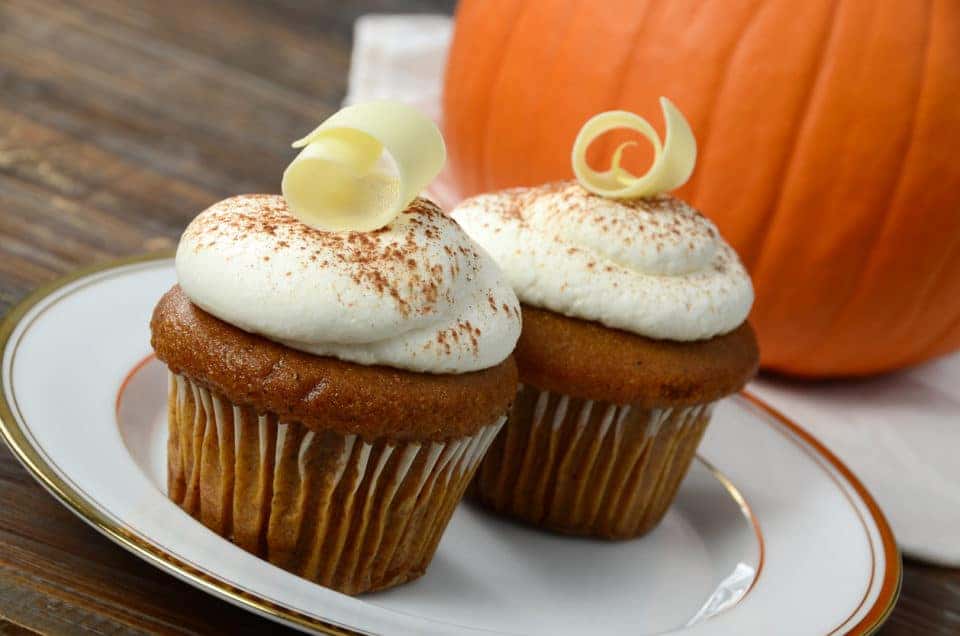 Two pumpkin cupcakes on a plate next to a pumpkin in the background