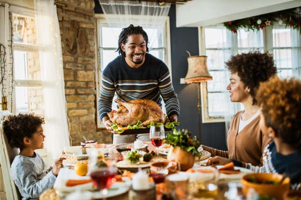 Happy black father bringing Thanksgiving turkey to the table.