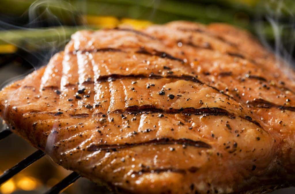 Close up of a grilled salmon filet on charcoal grill with asparagus