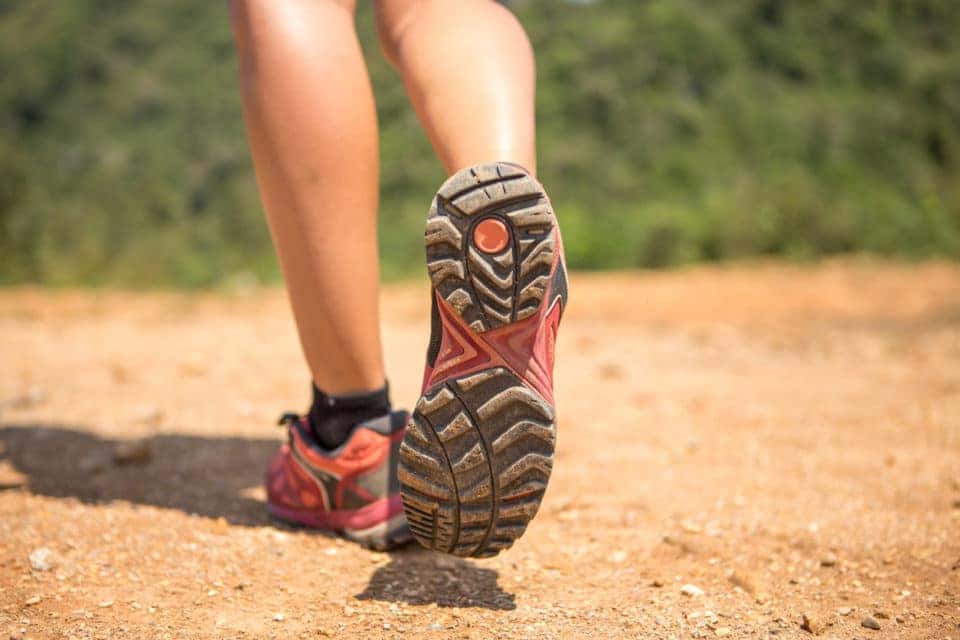 Legs and feet in pink hiking shoes walking and trekking on a red dirt.